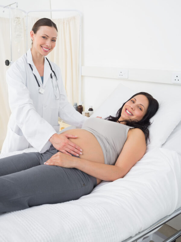 Portrait of happy female doctor with pregnant woman in examination room at hospital