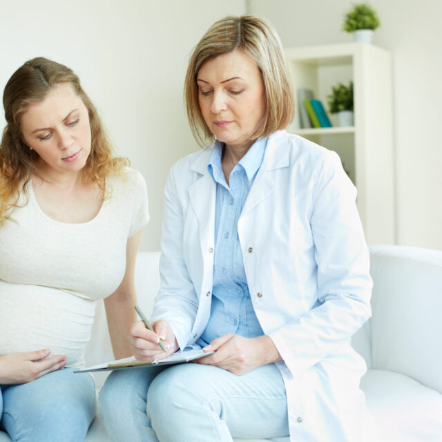 Young pregnant woman listening to prescription of doctor after regular examination at hospital