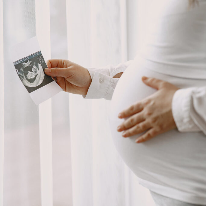 Woman standing by the window. Pregnant looking at photo. Woman expecting a baby.